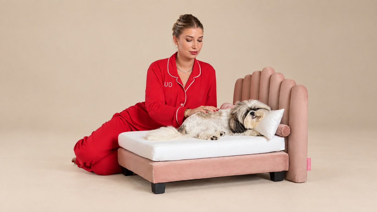 A Dusky Pink Luxor on a neutral studio backdrop, an owner beside a Shih Tzu asleep on the white bedding